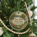 A round ornament hanging on a Christmas tree, featuring a scenic landscape with a lake and mountains.