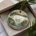 A decorative ornament in a box, featuring a scenic image of Deer Lake State Park, Florida.