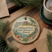 A decorative ornament featuring a tropical landscape with a mountain, palm trees, and a body of water, hanging on a wooden surface.