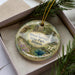 A decorative ornament with a scenic image of Dixon Springs State Park, Illinois, displayed in a box with pine branches.