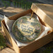 An ornament in a box, featuring a scenic landscape with a waterfall and greenery, with the text "Don Carter State Park, Georgia" displayed on it.