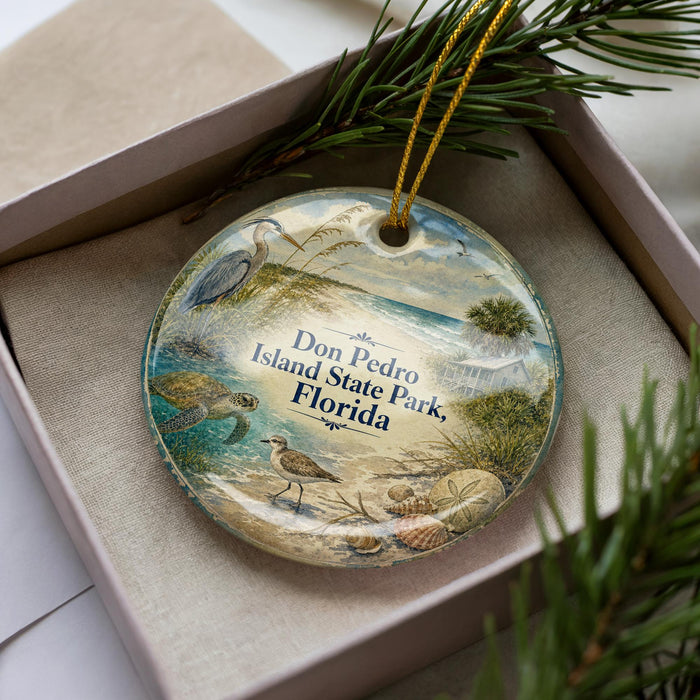 A decorative ornament in a box, featuring a beach scene with a bird, turtle, and palm tree.