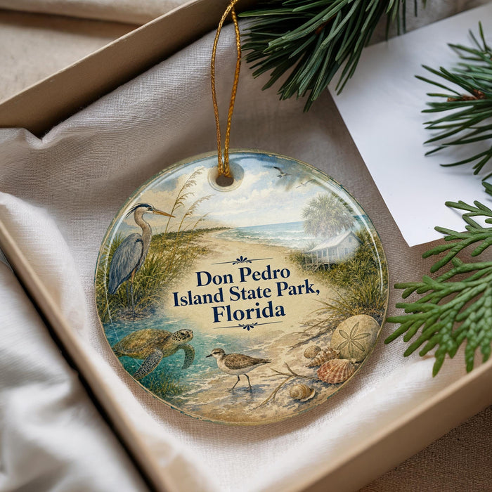 A decorative ornament with a beach scene and various sea birds, placed in a box with pine branches.