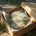 An oval ornament in a brown box, featuring a beach scene with a bird, turtle, and palm tree.