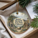 A decorative ornament with a scenic landscape of Donner Memorial State Park, California, featuring a wagon and a cabin, is displayed in a box with pine branches.