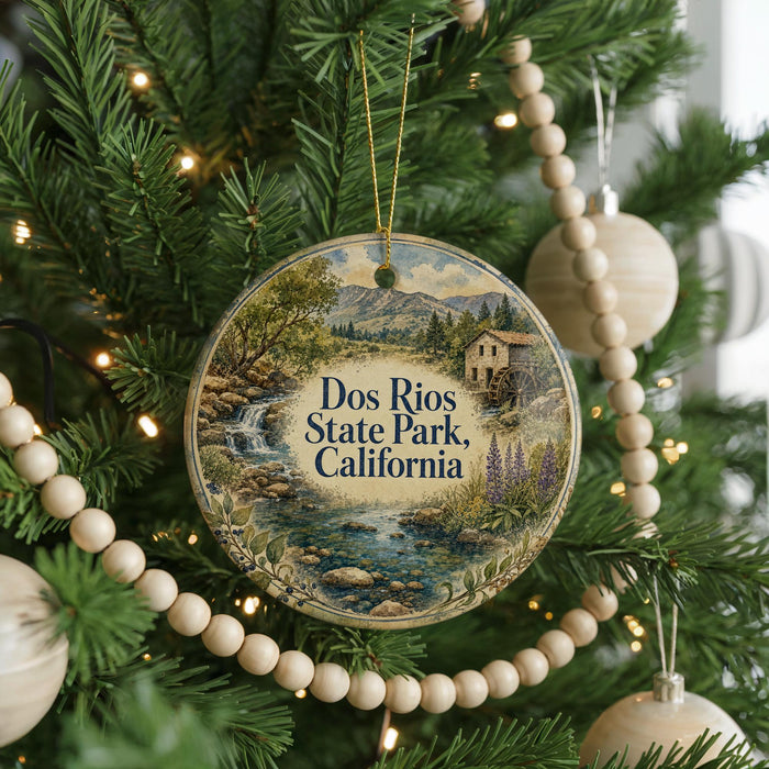 A round ornament hanging on a Christmas tree, featuring a scenic landscape with a waterfall and a house.