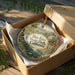 A decorative ornament in a box, featuring a scenic landscape with a river and mountains, with the text "Dos Rios State Park, California" prominently displayed.