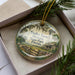 A decorative ornament in a box, featuring a scenic image of Dudley Farm Historic State Park, Florida.
