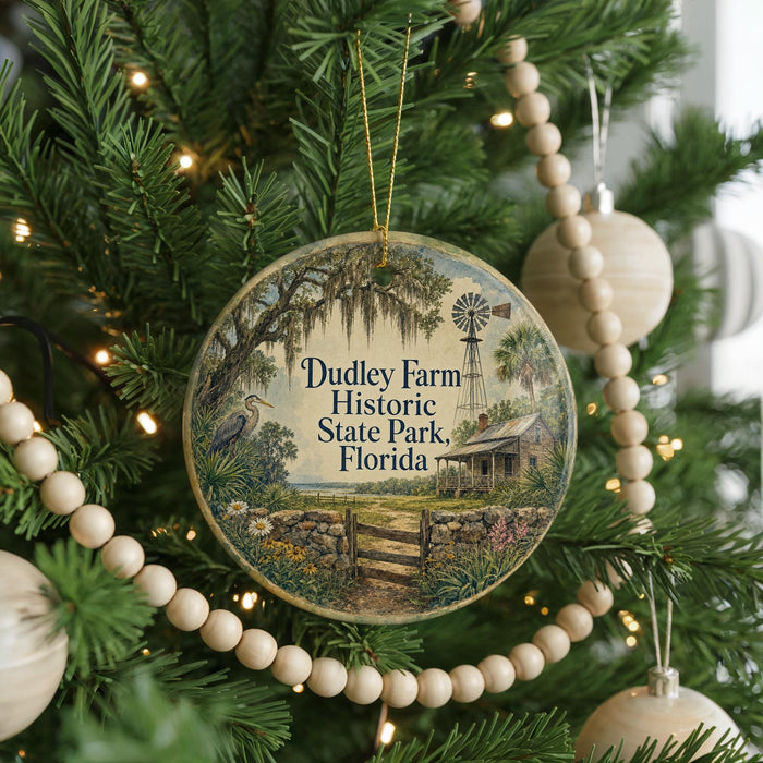 A round ornament hanging on a Christmas tree, featuring a scenic image of Dudley Farm Historic State Park, Florida.