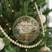 A round ornament hanging on a Christmas tree, featuring a scenic image of Dudley Farm Historic State Park, Florida.
