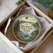 A decorative ornament in a box, featuring a scenic landscape with a lake, mountains, and a deer.
