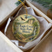 A round ornament with a bird and a waterfall, placed in a box with a white tissue paper lining.