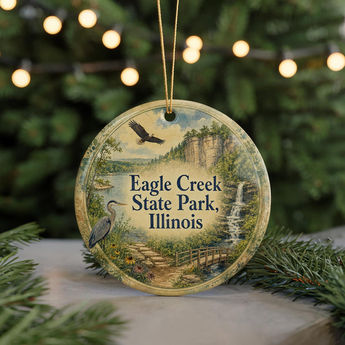 A round ornament with a scenic image of Eagle Creek State Park, Illinois, featuring a bird, a waterfall, and a bridge.