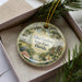 A decorative ornament in a box, featuring a scenic image of Eden Gardens State Park in Florida.