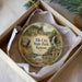A decorative ornament in a box, featuring a scenic landscape with a waterfall, a cabin, and a deer.