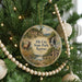 A round ornament hanging on a Christmas tree, featuring a scenic landscape with a deer, a waterfall, and a cabin.