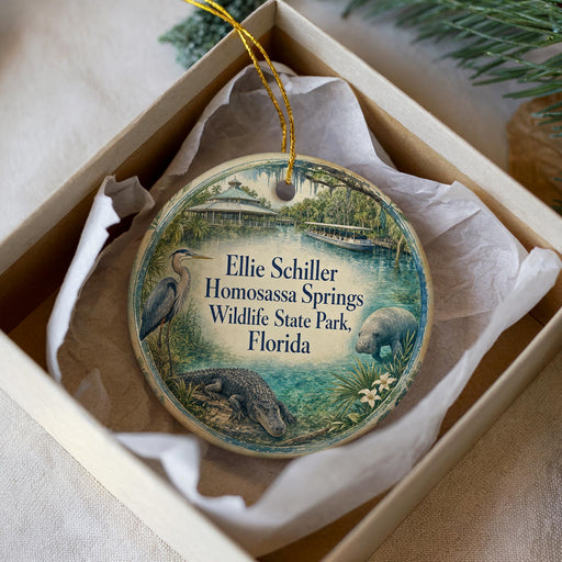 A decorative ornament in a white box, featuring an illustration of a bird, a manatee, and a beaver, along with text that reads "Ellie Schiller Homosassa Springs Wildlife State Park, Florida".