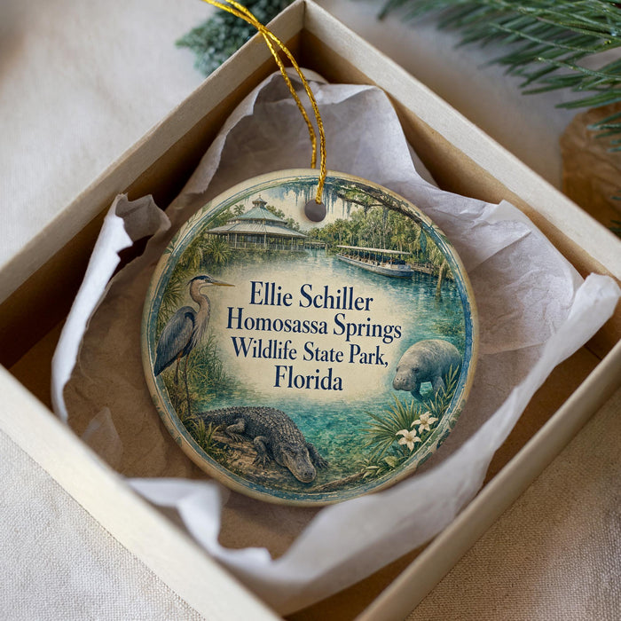 A decorative ornament in a white box, featuring an illustration of a bird, a manatee, and a beaver, along with text that reads "Ellie Schiller Homosassa Springs Wildlife State Park, Florida".