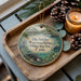 A wooden tray with a decorative ornament featuring a bird, a beaver, and a waterfowl, along with pine cones and a lit candle.