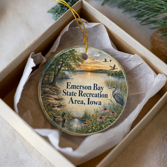 A decorative ornament in a box, featuring a scenic landscape with a lake, trees, and birds.