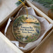 A decorative ornament in a box, featuring a scenic landscape with a lake, trees, and birds.