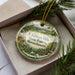 A decorative ornament in a box, featuring a scenic landscape of the F. Gilbert Hills State Forest in Massachusetts.