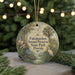 A round ornament with a tropical scene, featuring a bird, palm tree, and water, hangs in front of a blurred background with Christmas lights.