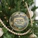 A round ornament hanging on a Christmas tree, featuring a scenic landscape with mountains, pine trees, and a lake.