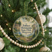 A round ornament hanging on a Christmas tree, featuring a scenic landscape with a waterfall and a house.