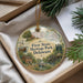 A decorative ornament with a painting of historic buildings and people, placed in a box with pine branches.