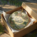 A wooden box containing a decorative ornament with illustrations of historic buildings and people, labeled as "First State Heritage Park, Delaware".
