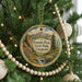 A round ornament hanging on a Christmas tree, featuring a scenic mountain landscape with a waterfall.