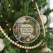 A round ornament hanging on a Christmas tree, featuring a scenic image of Fondahebeau State Park in Louisiana.