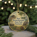 A round ornament with a painting of a fort, barn, and wagon, surrounded by greenery and a string of lights.