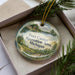 A decorative ornament in a box, featuring a scenic landscape with a lake and a small building.