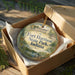 A round ornament in a box, featuring an illustration of Fort Harrison State Park, Indiana.