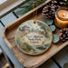 A decorative ornament featuring a painting of Fort Massac State Park in Illinois, with a candle and pine cones on a wooden tray.