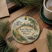 A round ornament featuring a painting of Fort Massac State Park, Illinois, with a boat and a building in the background.