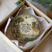 A round ornament with a painting of a historical scene, including a fort, palm trees, and a small boat, is displayed in a box.