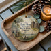 A decorative ornament featuring a scenic image of Fort Mose Historic State Park, Florida, with a candle and pine cones on a wooden tray.