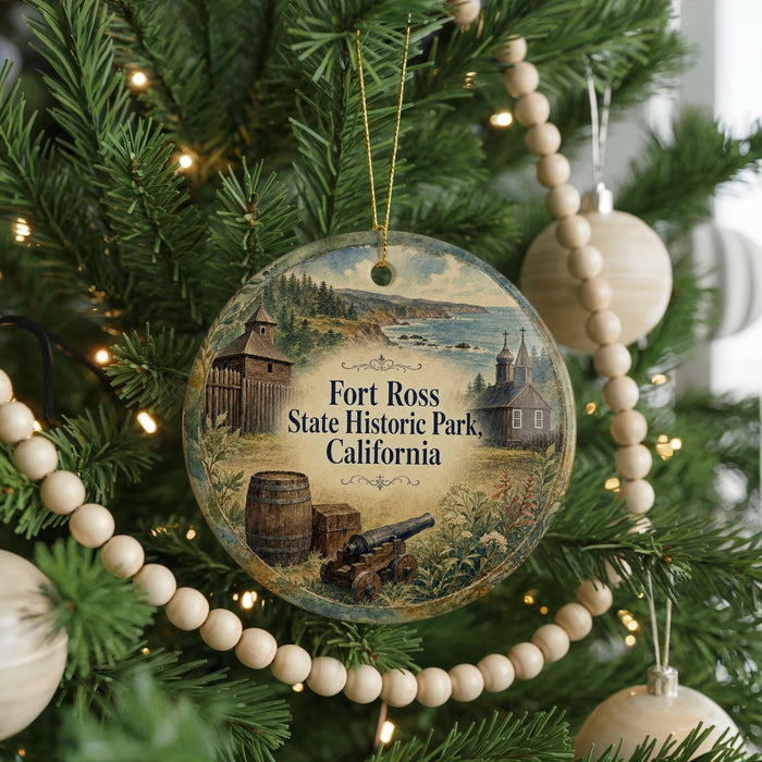 A round ornament hanging on a Christmas tree, featuring illustrations of a historical fort and a barrel, with the text "Fort Ross State Historic Park, California" displayed prominently.