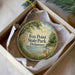 A round ornament in a box, featuring a scenic image of a fox in a field with a body of water in the background.
