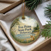 A decorative ornament with a fox standing on a beach, surrounded by pine trees and grass, is displayed in a box.