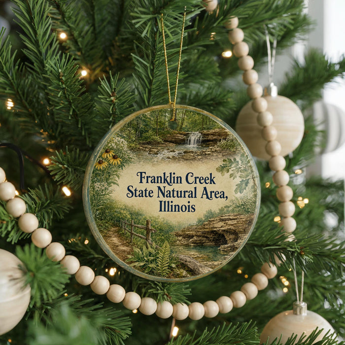 A round ornament hanging on a Christmas tree, featuring a scenic image of Franklin Creek in Illinois.