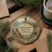 A decorative ornament with a scenic mountain landscape and the text "Fremont Peak State Park, California" is displayed on a wooden surface, accompanied by a cup of coffee and pine branches.