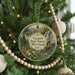 A round ornament hanging on a Christmas tree, featuring a scenic landscape with a waterfall, pine trees, and a cabin.