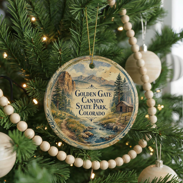 A round ornament hanging on a Christmas tree, featuring a scenic landscape with mountains, a river, and a cabin.