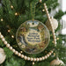 A round ornament hanging on a Christmas tree, featuring a scenic landscape with a waterfall, cabin, and deer.