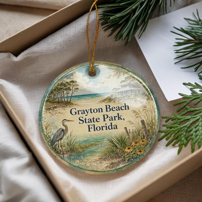 A round ornament with a beach scene and text, placed in a box with pine branches.