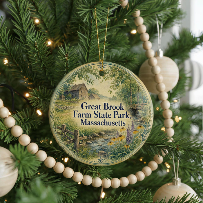 A round ornament hanging on a Christmas tree, featuring a scenic image of a farm and a stream.